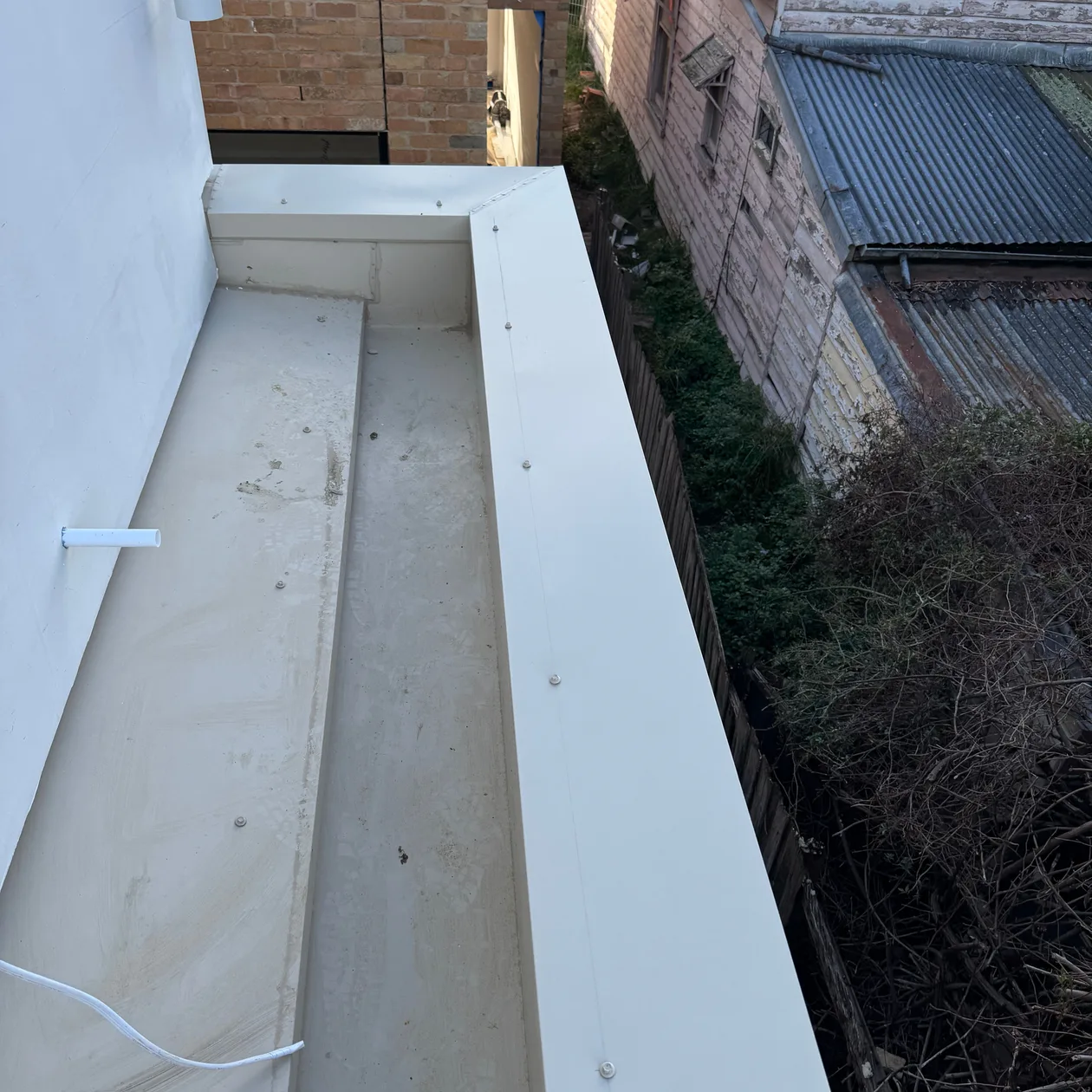 New metal box gutter being installed beside a wall, work in progress