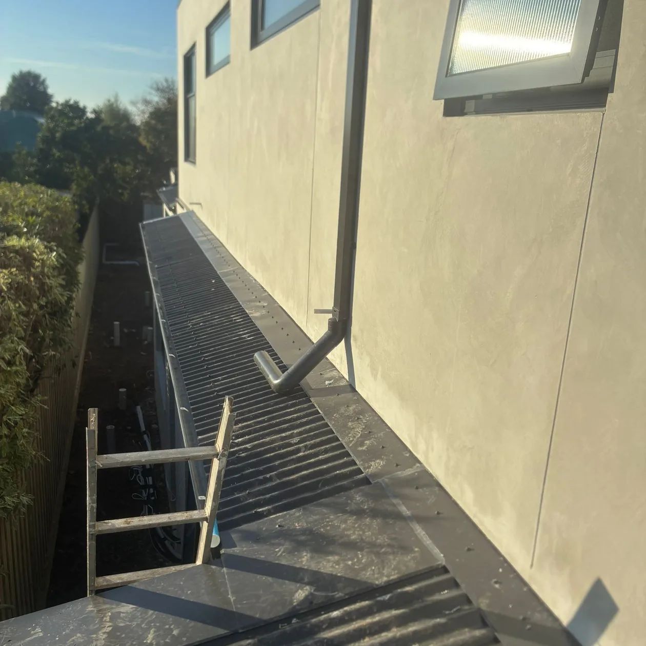 Metal box gutter running along a rendered wall with a downpipe above it