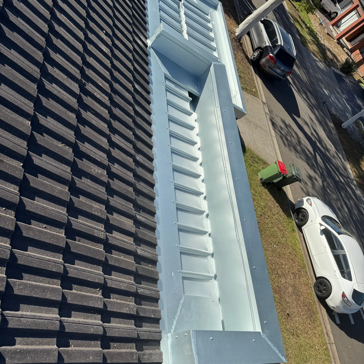 Metal box gutter with an outlet at one end running beside a dark tiled roof