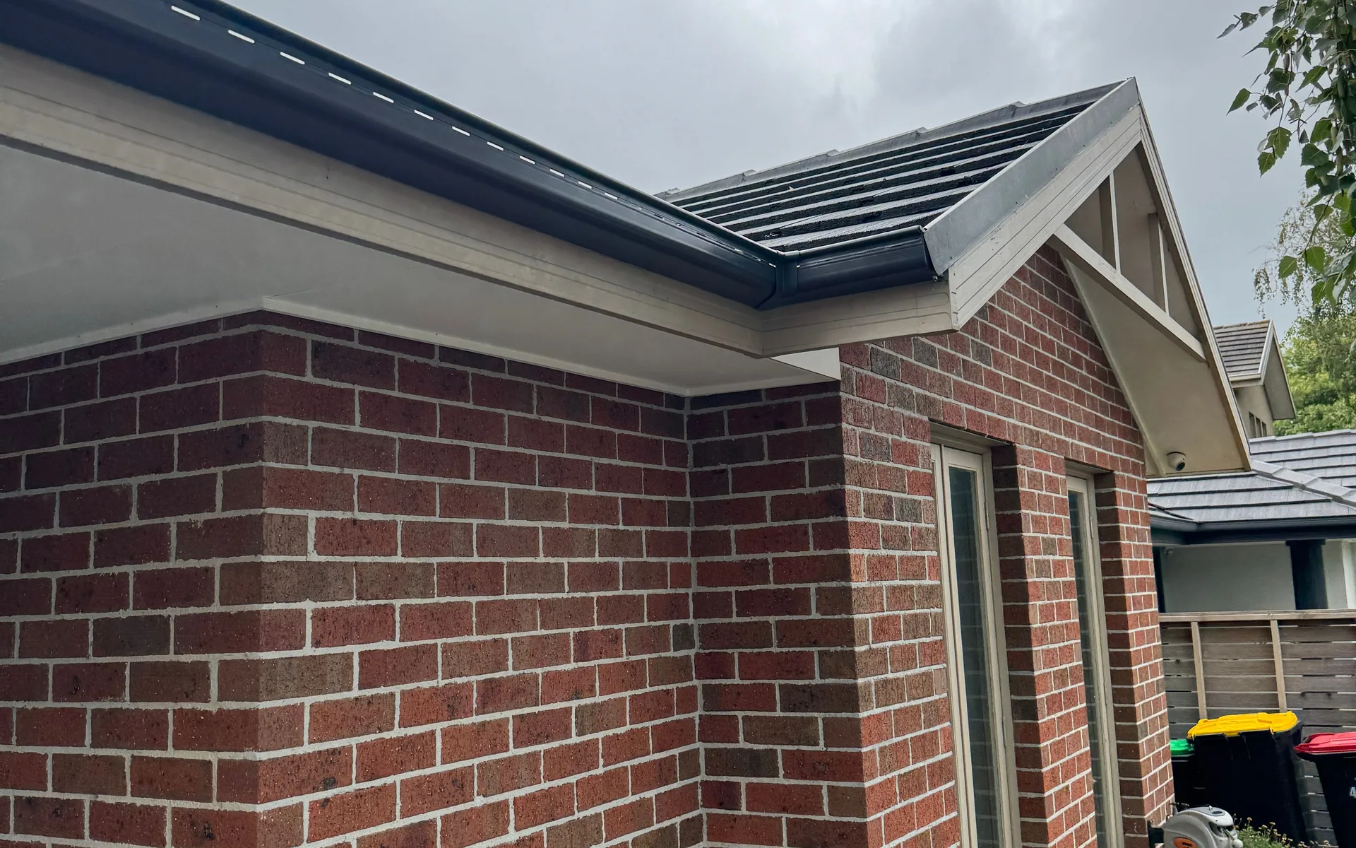Red brick home with dark fascia and gutter running along the eaves under a tiled roof