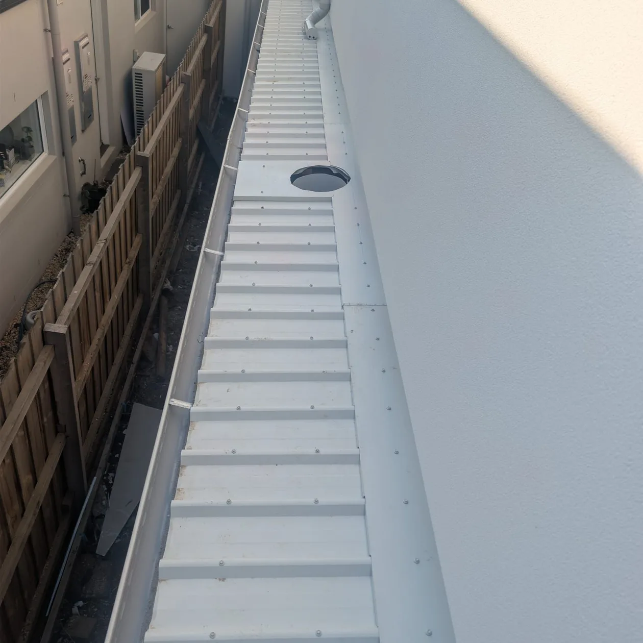 Clean pale metal box gutter with an outlet, running beside a rendered wall