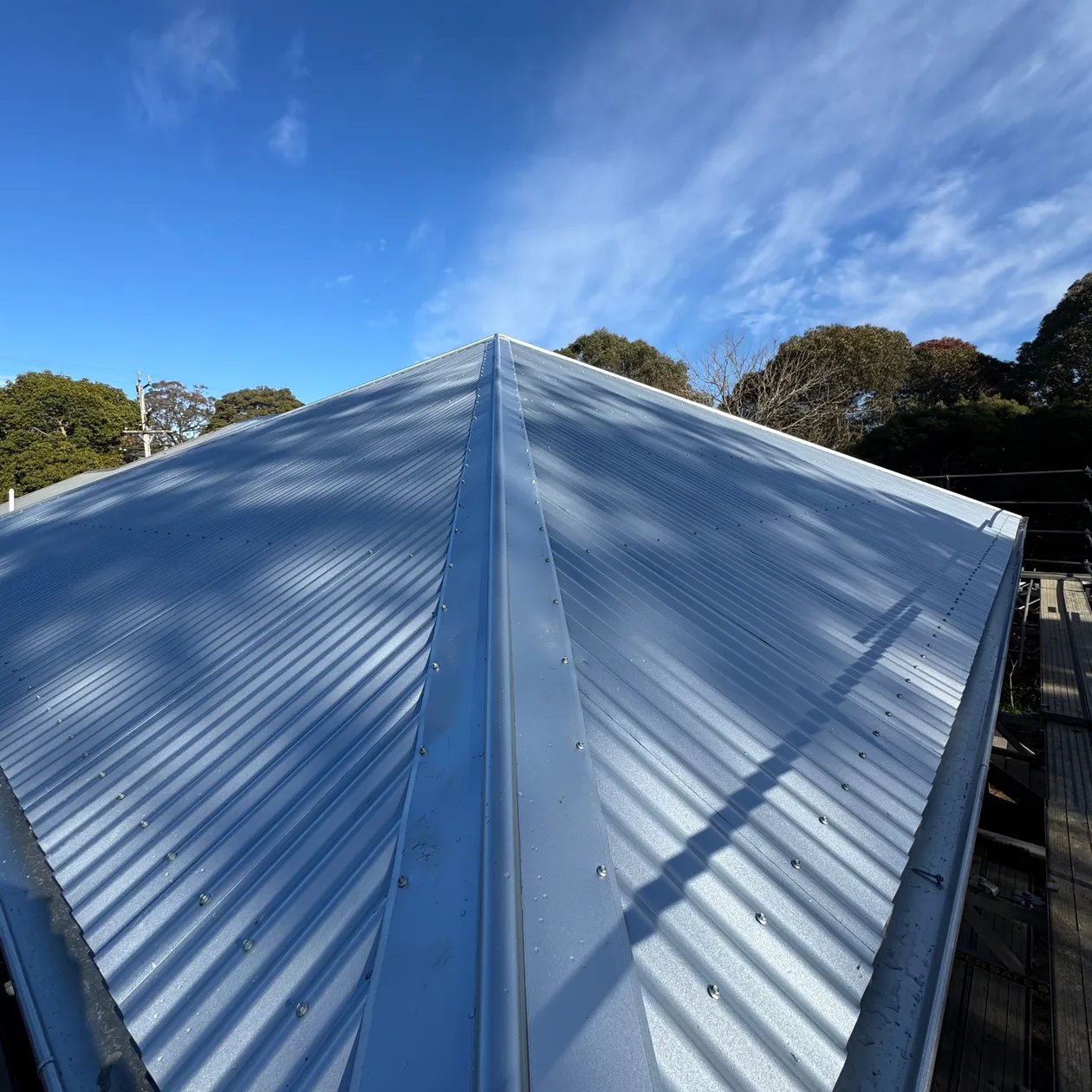 Ridge line of a grey corrugated metal roof against a blue sky