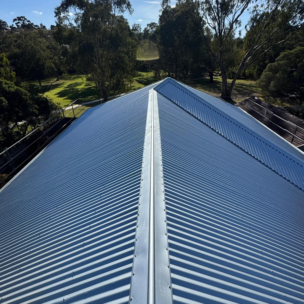 Corrugated metal roof ridge with treetops behind
