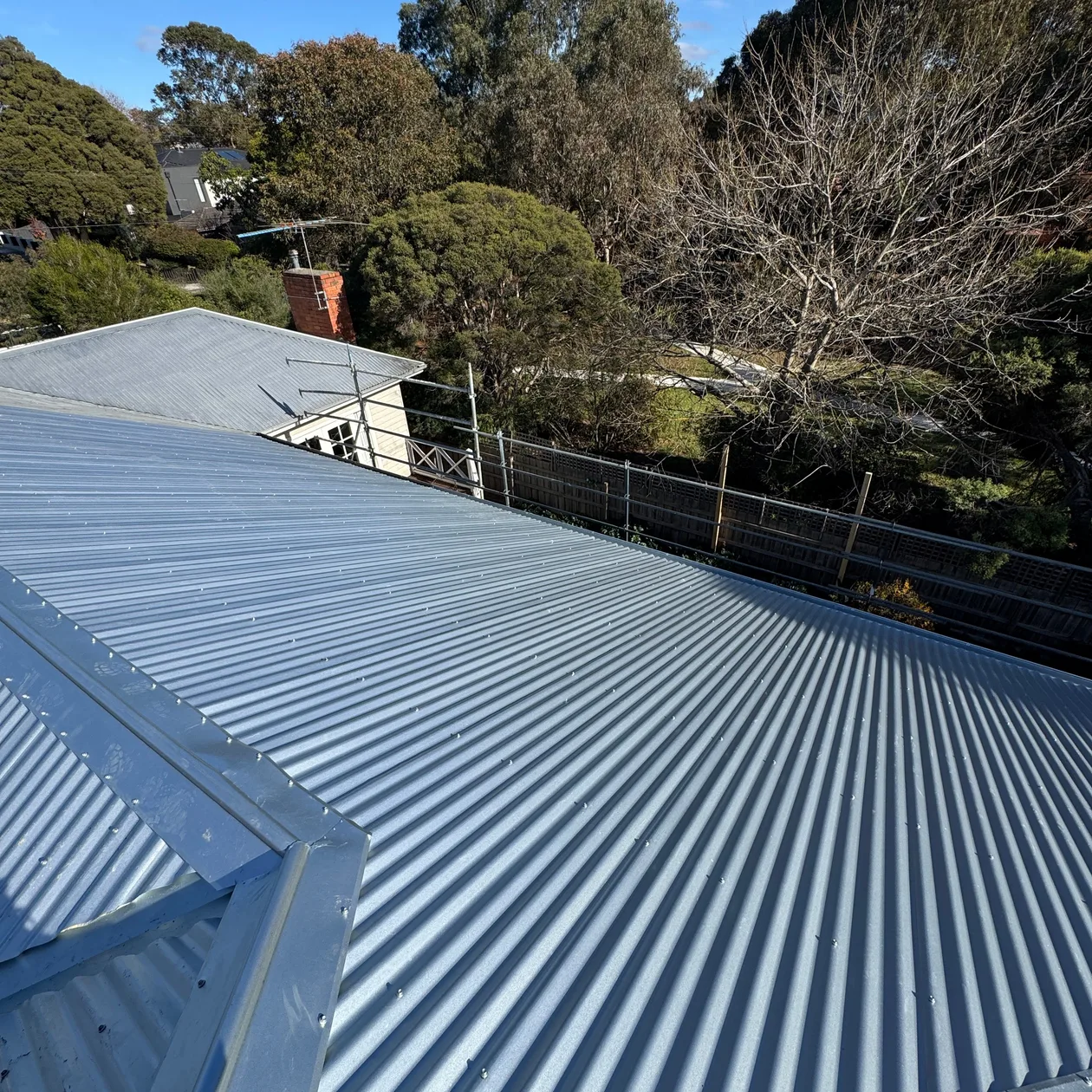 Corrugated metal roof with a metal edge detail, surrounded by trees and neighbouring roofs