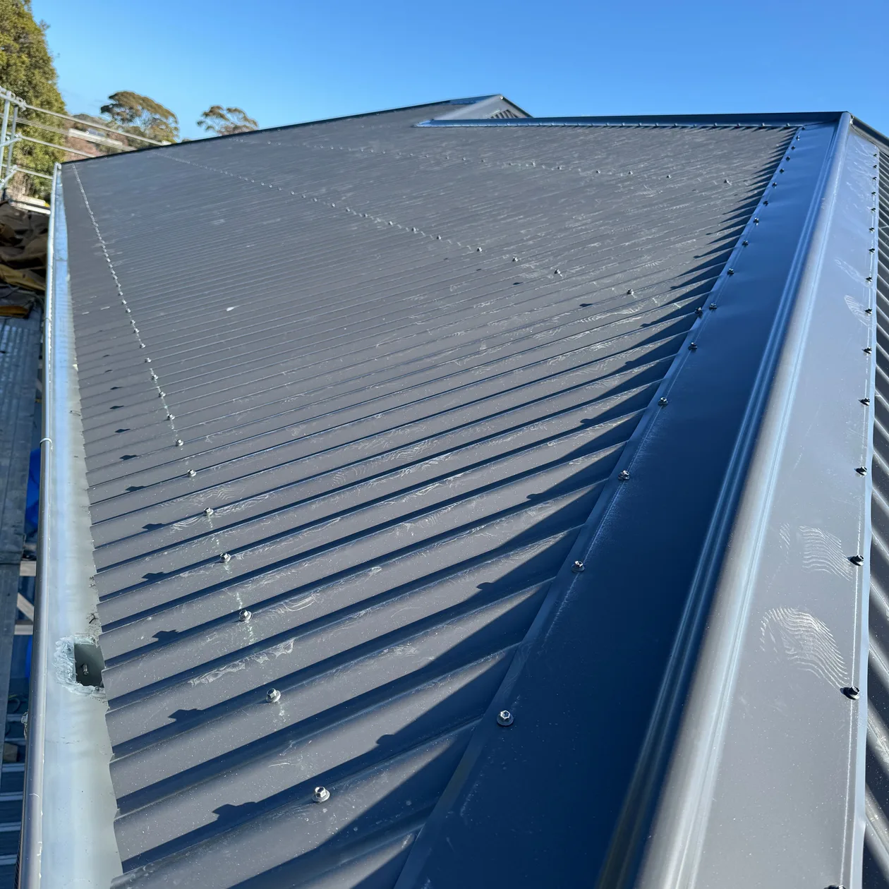 Gutter running along the lower edge of a dark corrugated metal roof under a blue sky