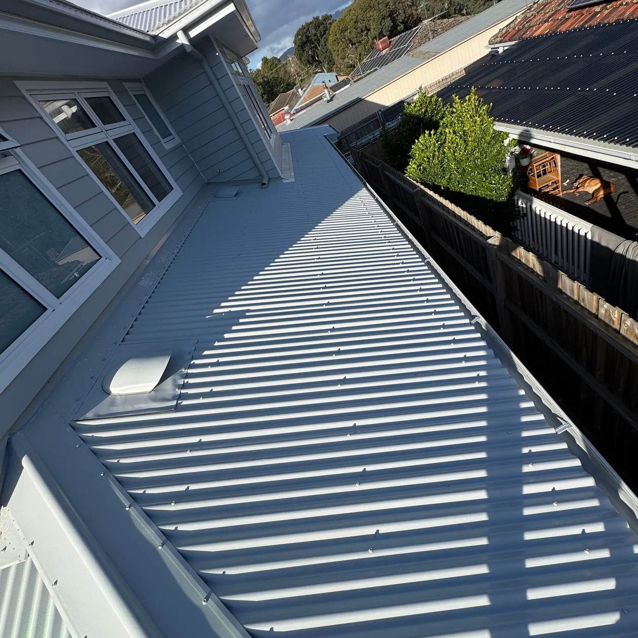 Grey corrugated metal roof running alongside a weatherboard wall and timber fence