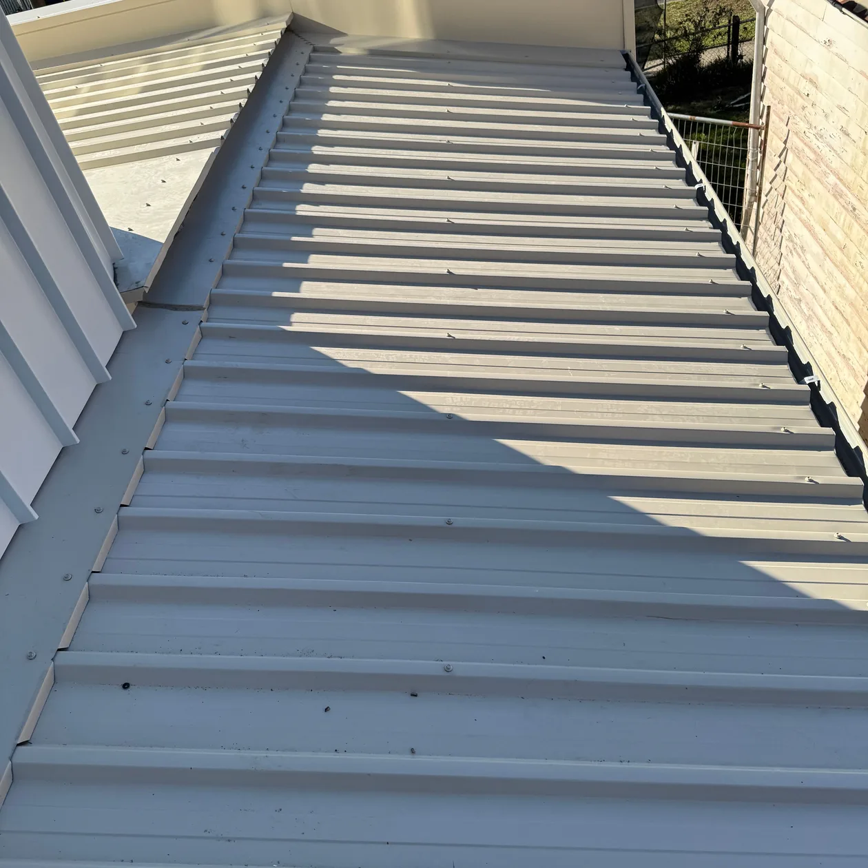 Sunlit corrugated metal roof running between two walls