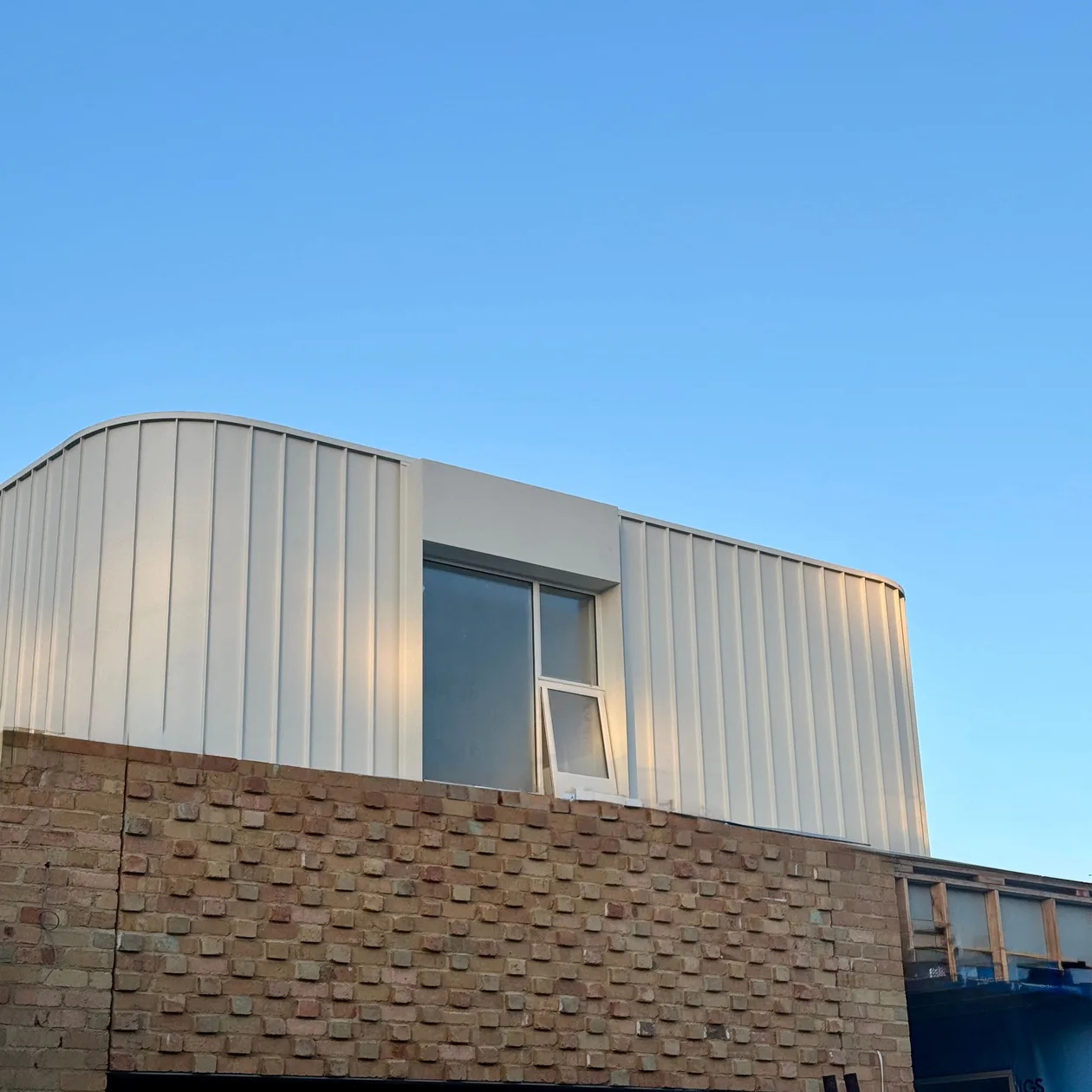 White metal cladding with a curved top edge on an upper storey above a brick home