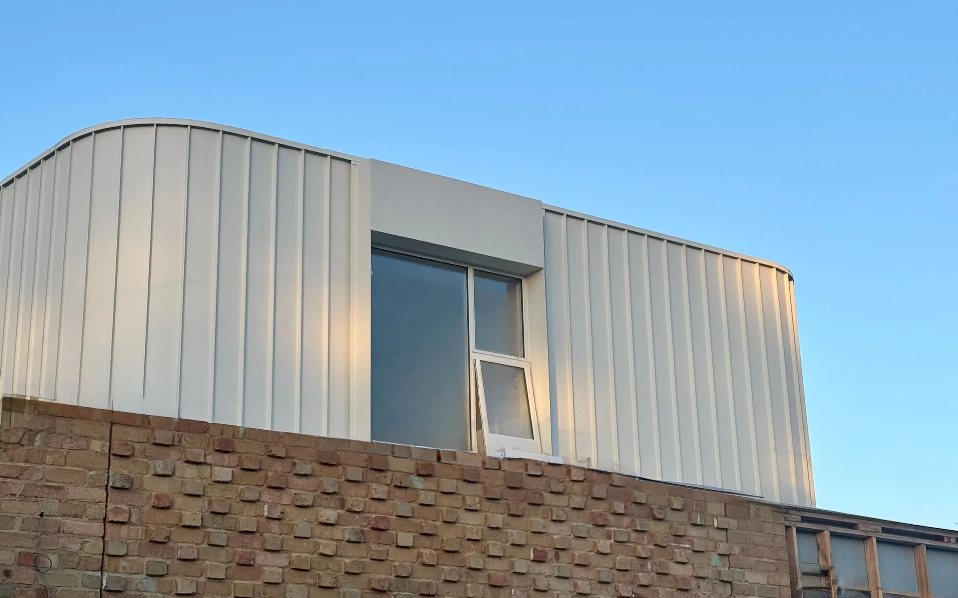 Curved vertical metal cladding wrapping an upper storey above textured brickwork