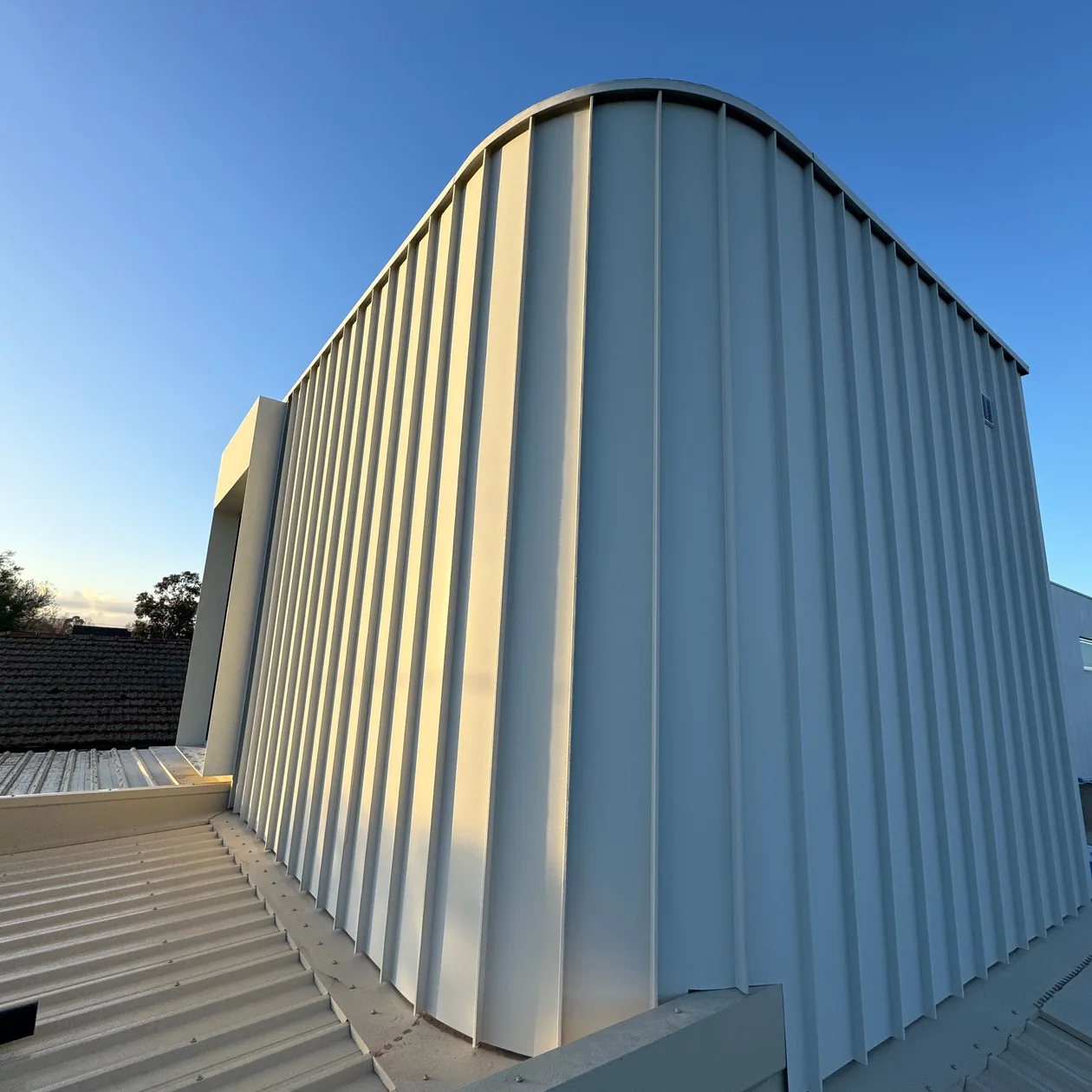 Pale vertical metal cladding curving over the top of a modern upper storey