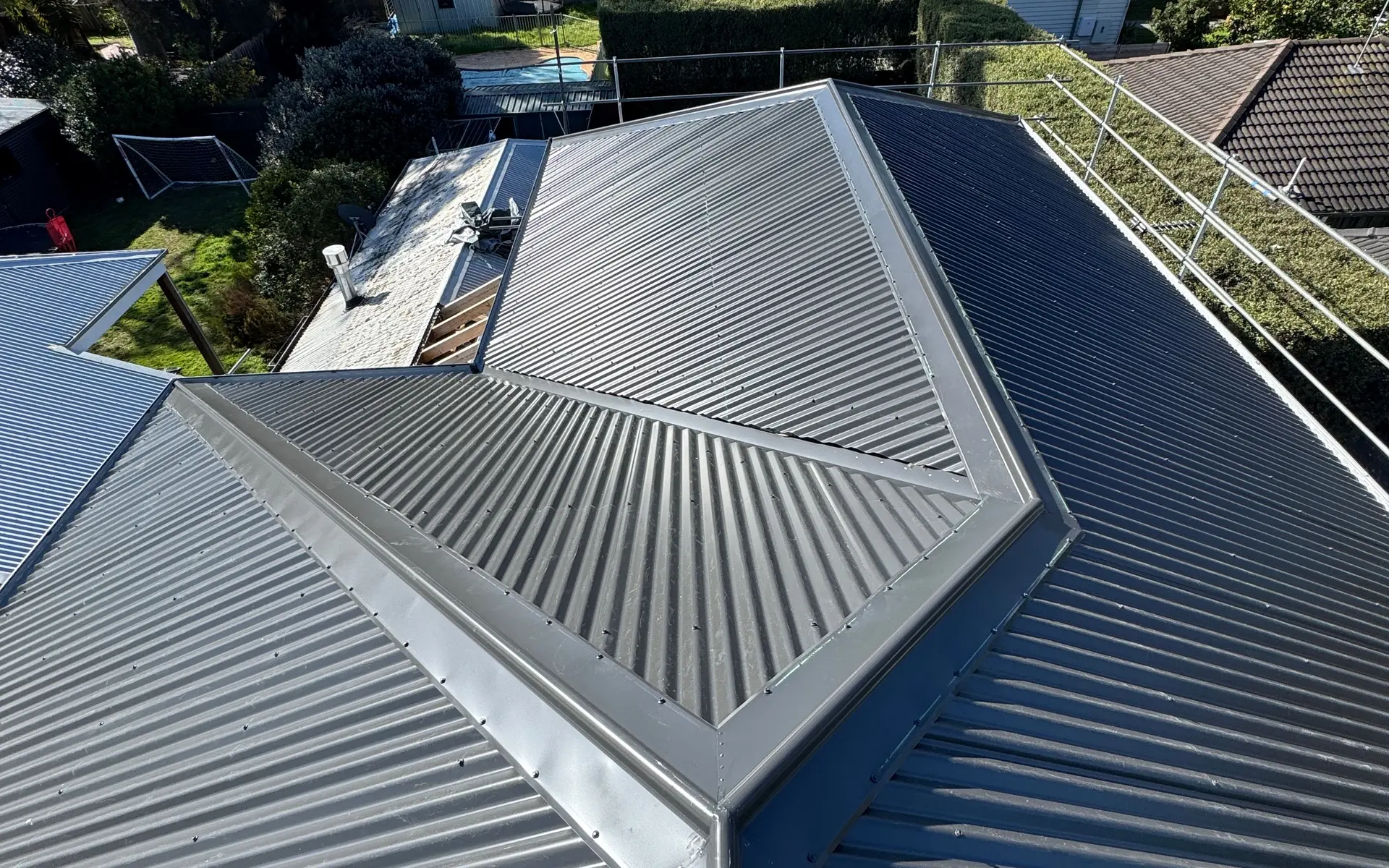 Dark corrugated metal hip roof above a suburban backyard