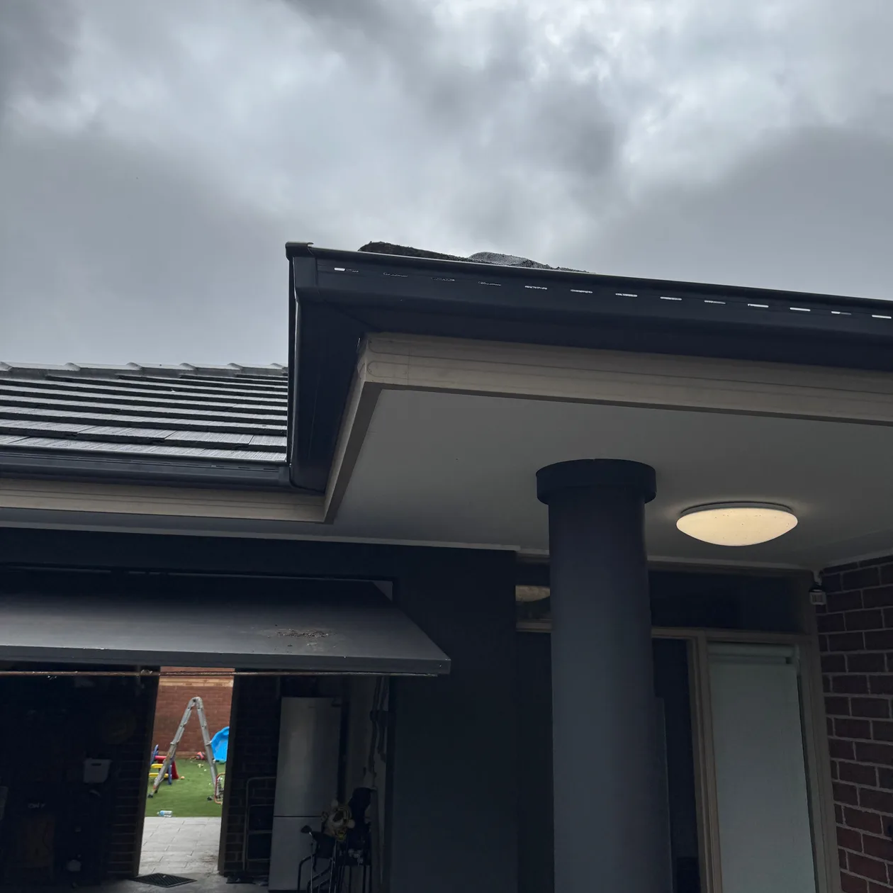 Dark fascia and gutter along the eaves of a home with a dark tiled roof and front porch