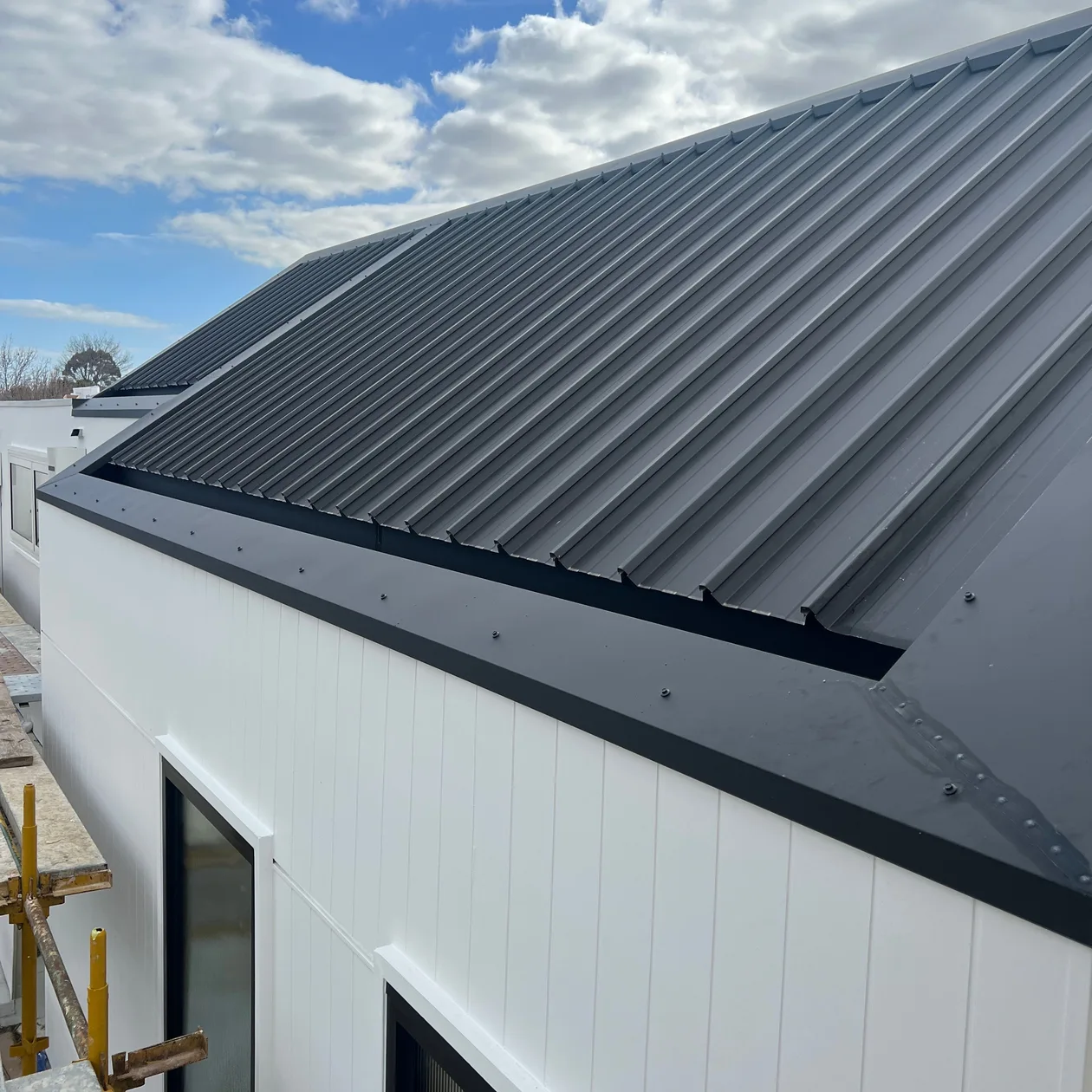 Dark metal roof edge above white wall cladding on a new home