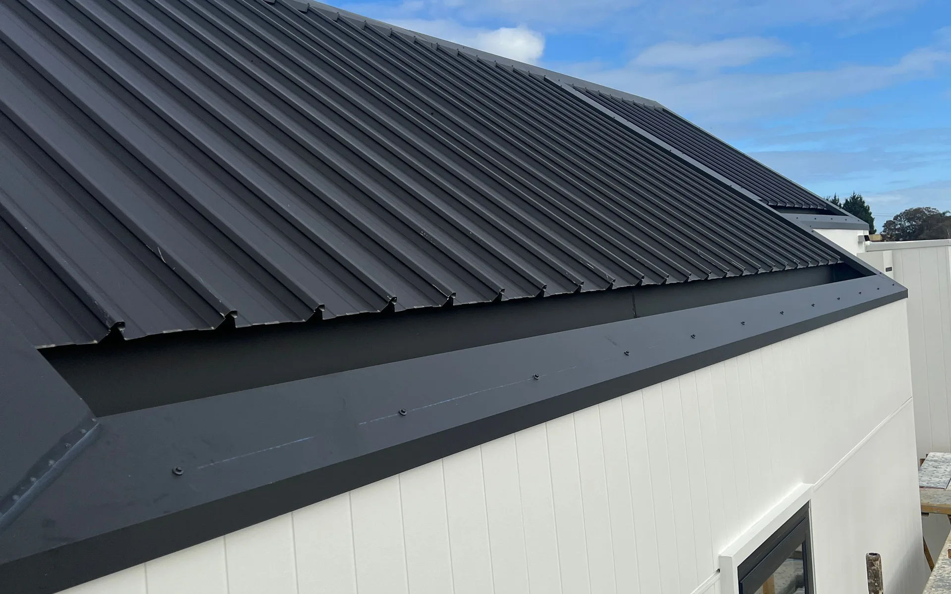 White vertical metal wall cladding beneath a dark metal roof edge on a new home