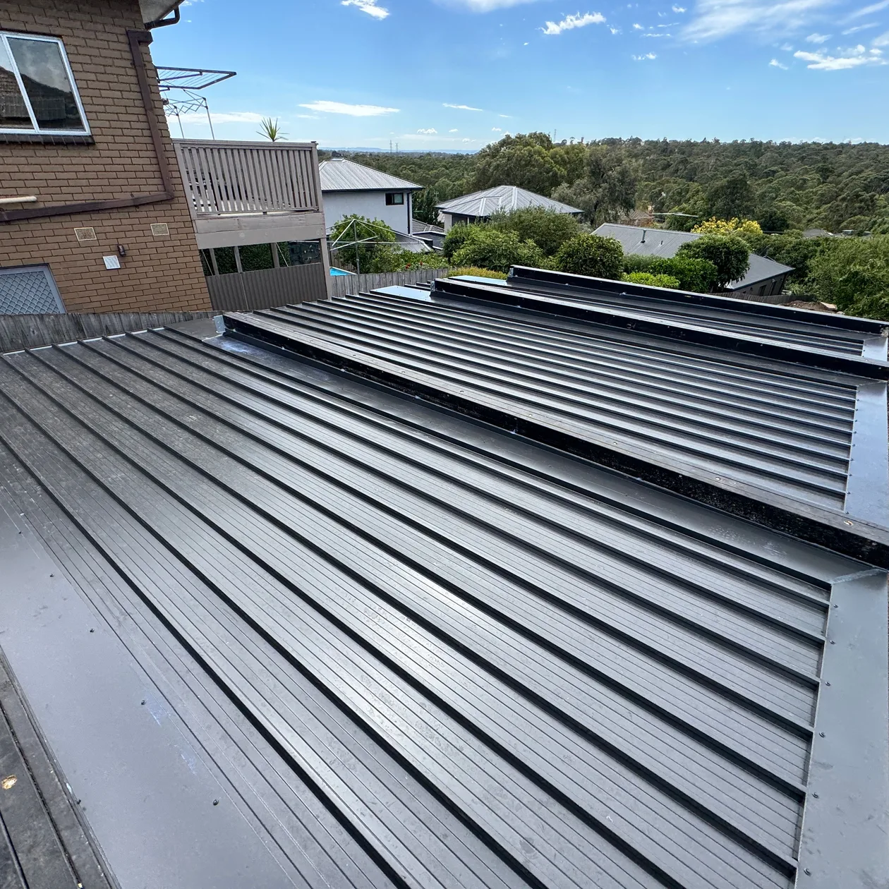 Dark standing seam metal roof running alongside a brick wall