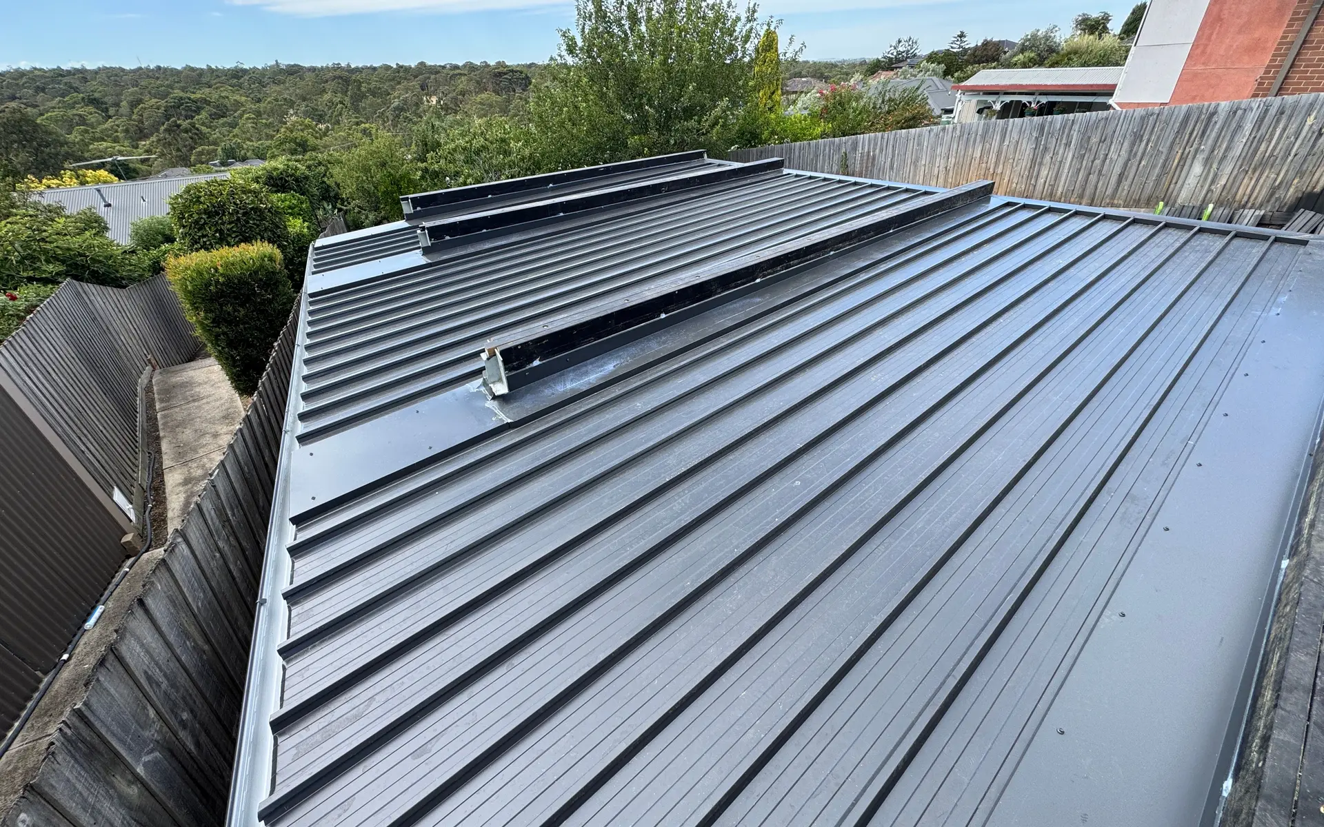 Dark standing seam metal roof with a box gutter edge and treetops behind
