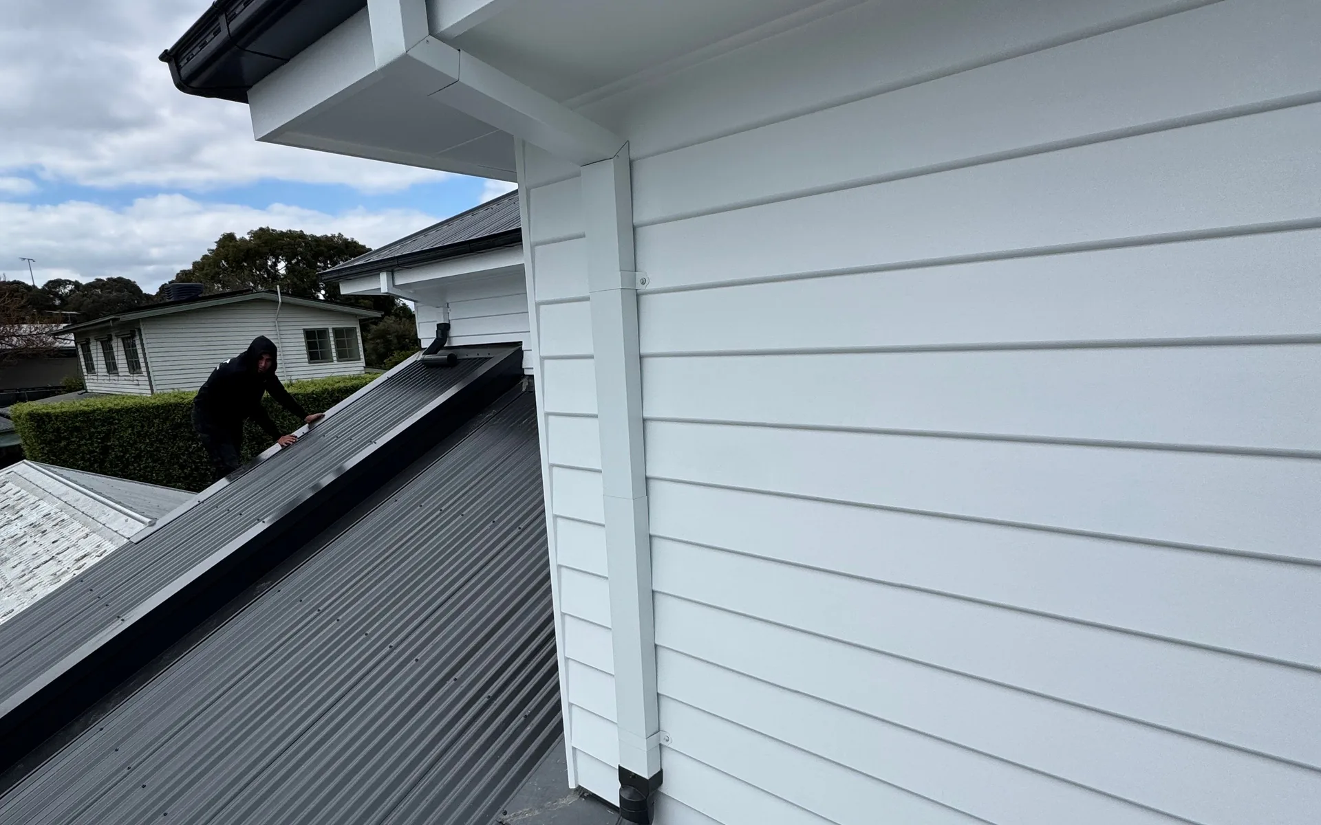 White gutter and downpipe on a weatherboard upper storey above a dark metal roof