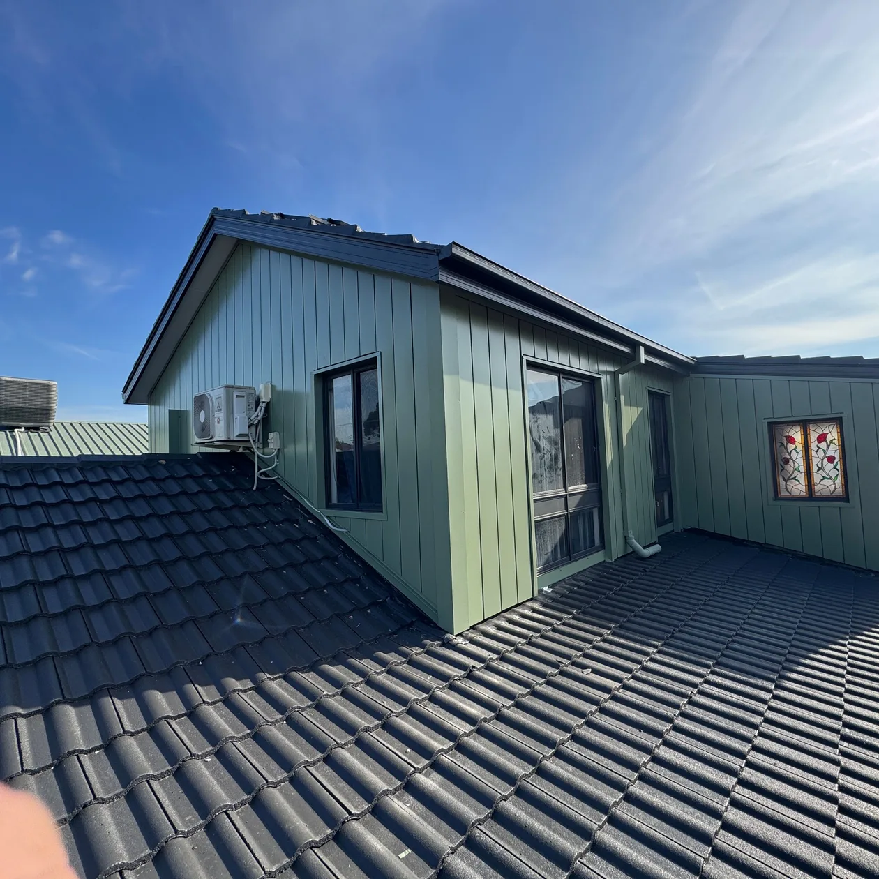 Green vertical metal cladding on an upper-storey addition above a tiled roof