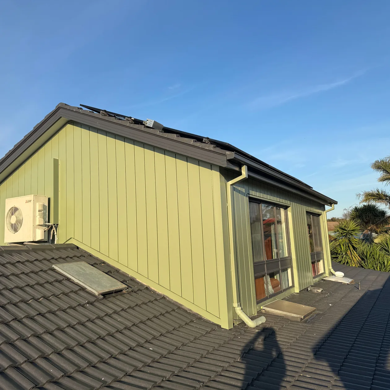 Green vertical metal cladding on a gable above a tiled roof