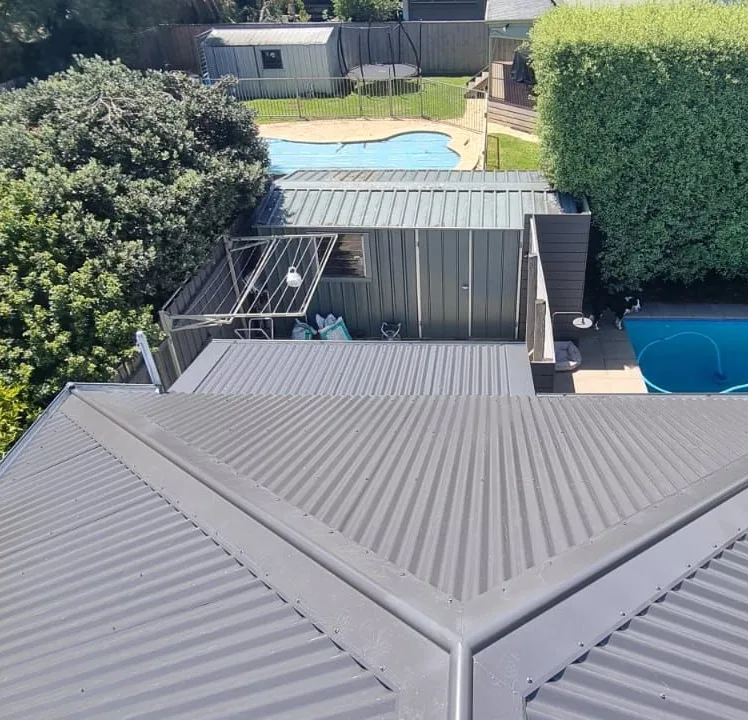 Dark metal hip roof beside a backyard swimming pool