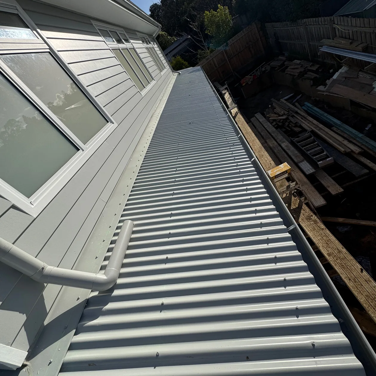 Long pale corrugated roof running beside a weatherboard wall, with a flashing along the wall