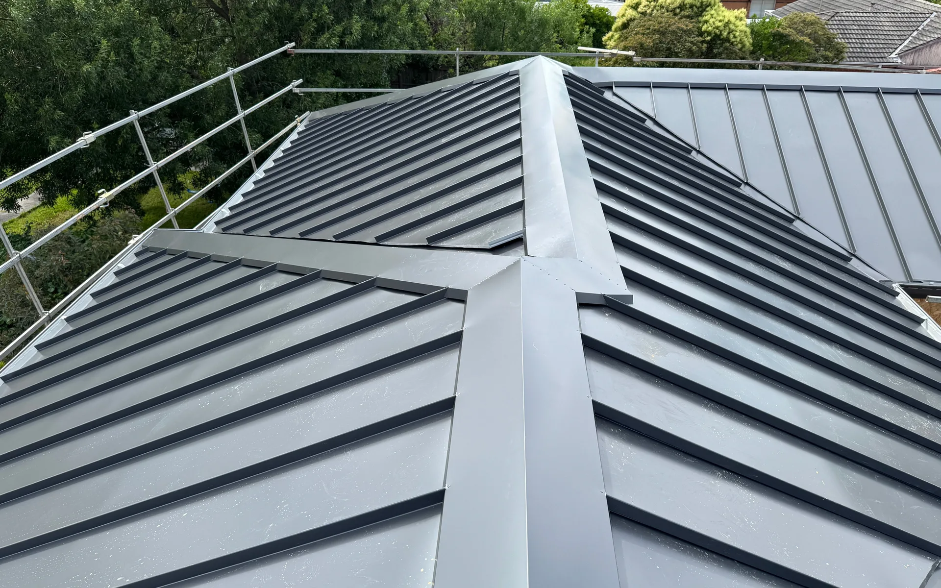Grey standing seam metal hip roof with a scaffold rail along the edge