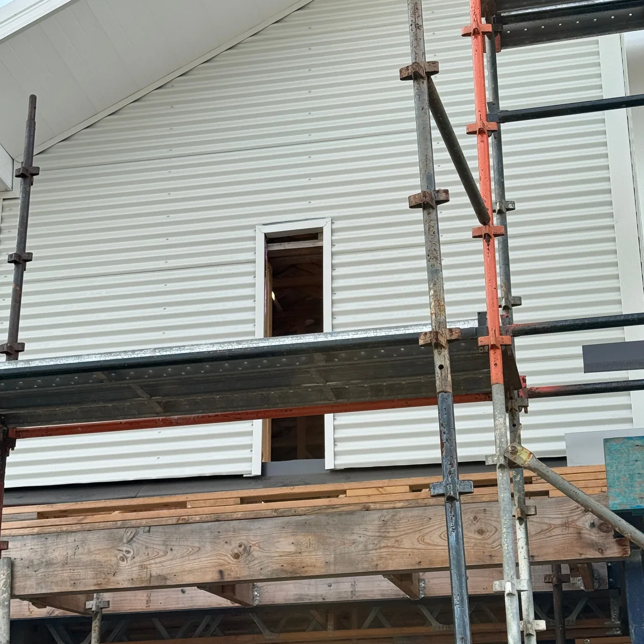 Wall cladding work in progress on a white gable, with scaffolding in place