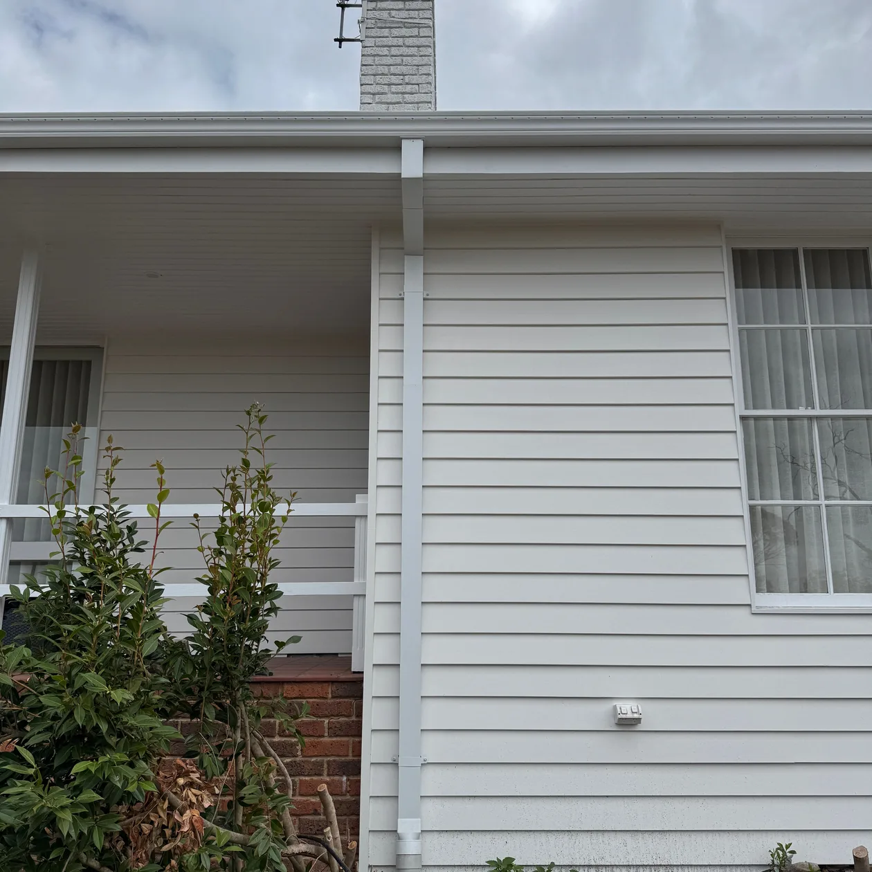 White gutter and downpipe on a weatherboard home beside the front verandah