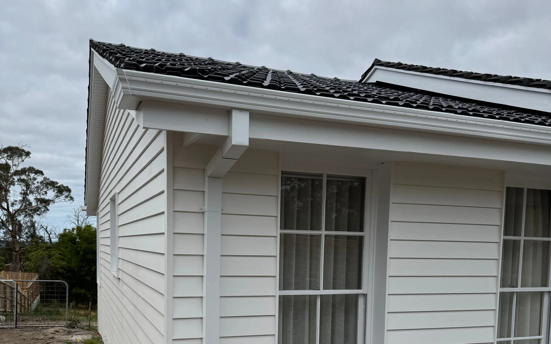 White gutter, fascia and downpipe on a weatherboard home with a dark tiled roof