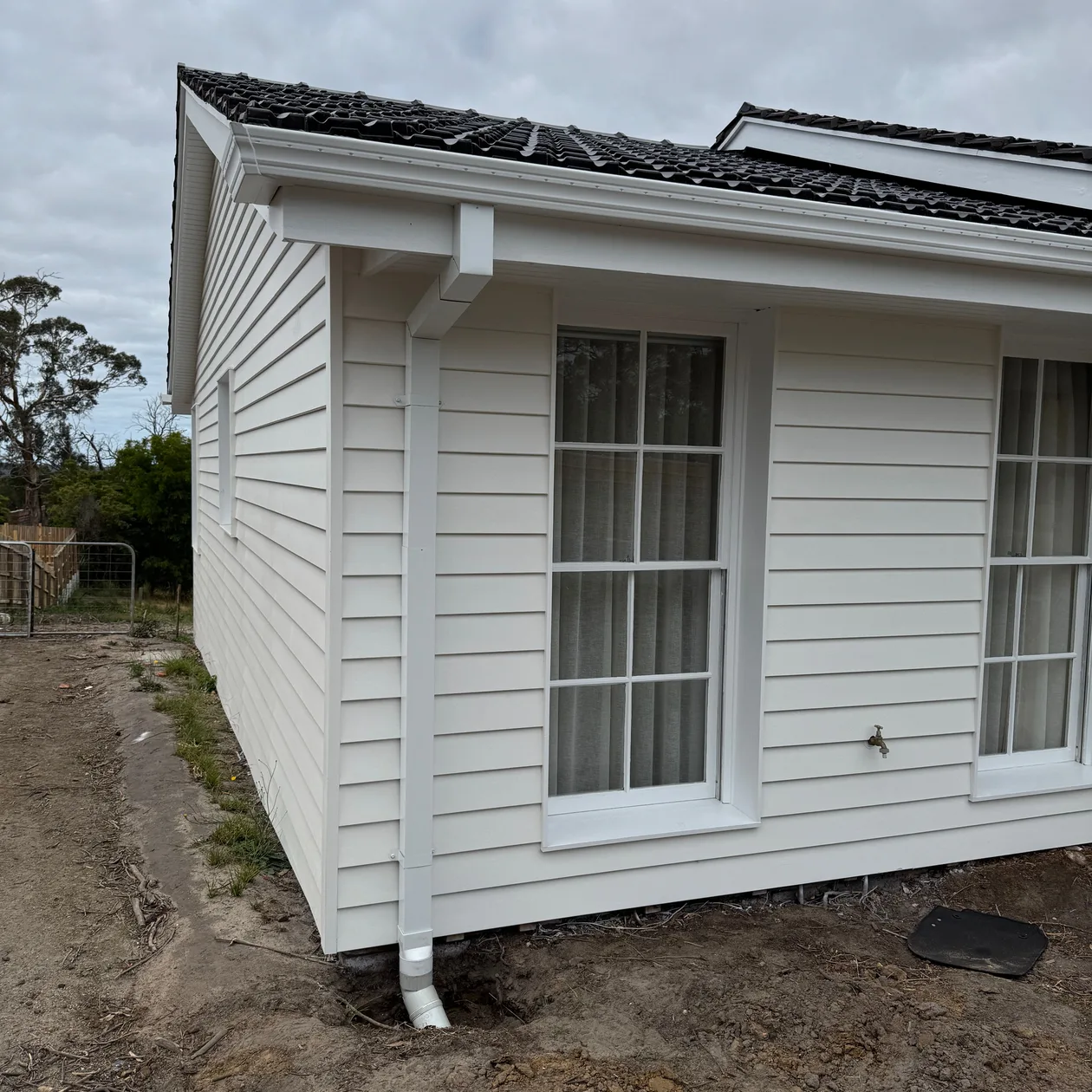 White weatherboard home with white fascia, gutter and downpipe under a dark tiled roof