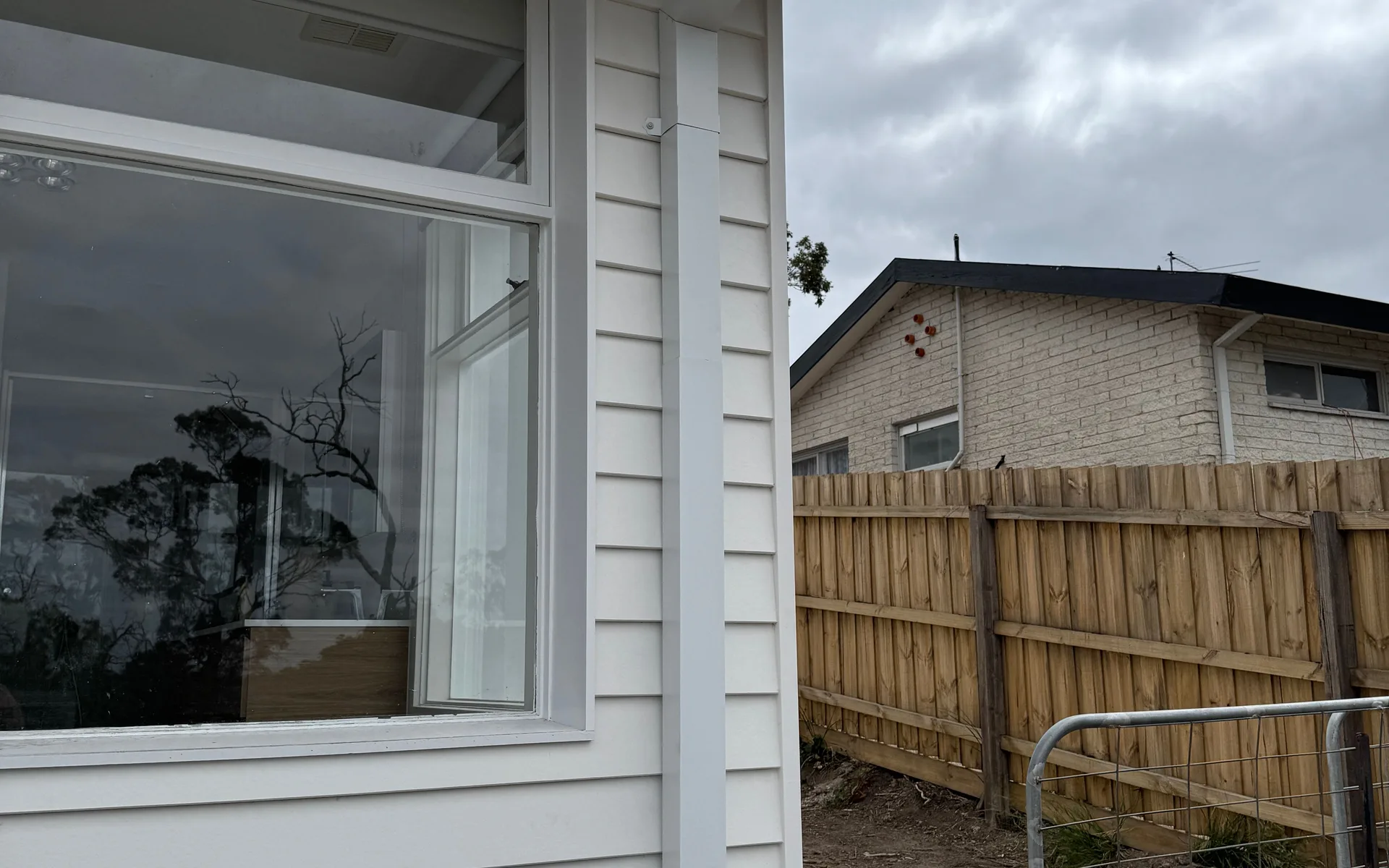 White downpipe running down the corner of a weatherboard home from the gutter above