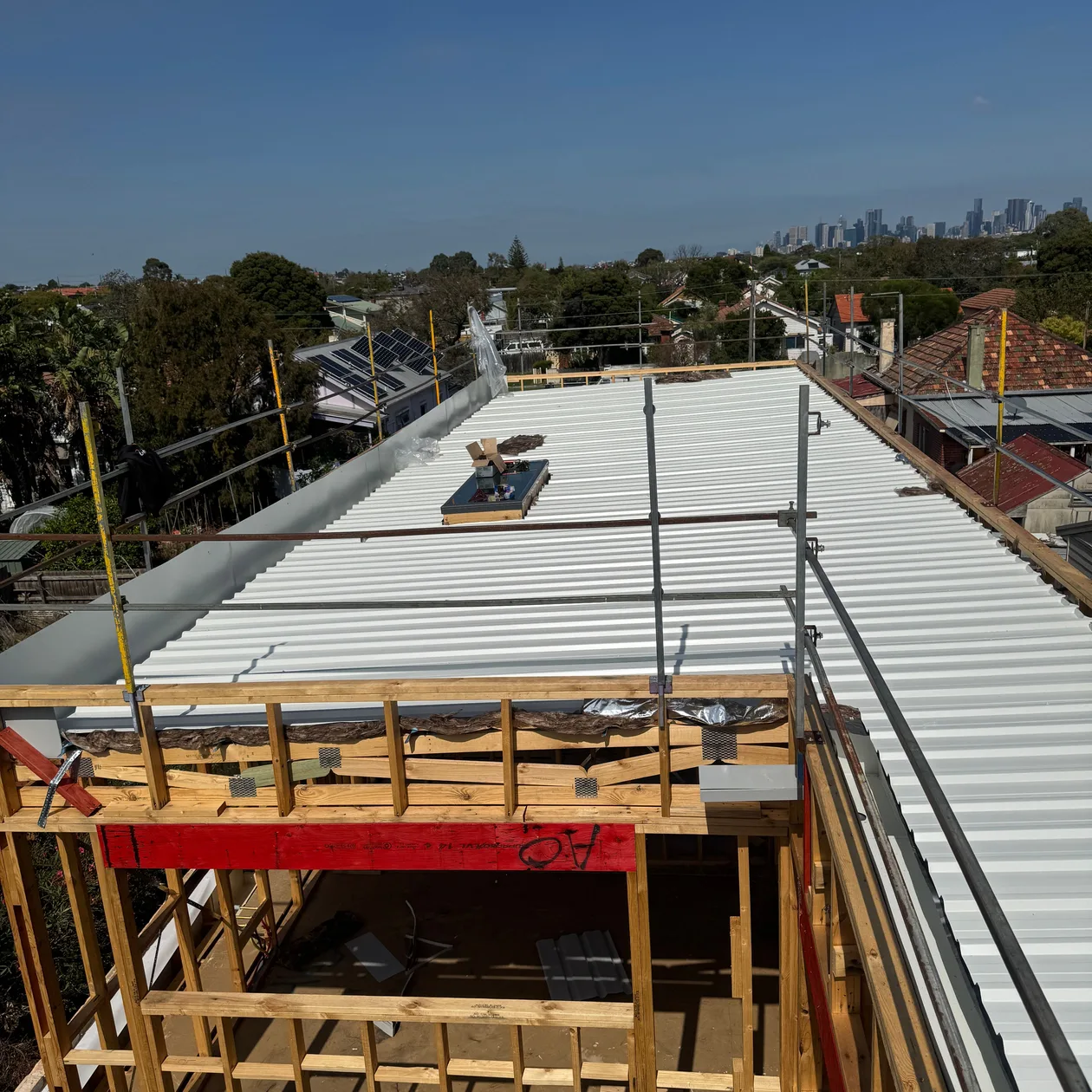 New pale metal roof going on over a timber frame, work in progress, city skyline in the distance