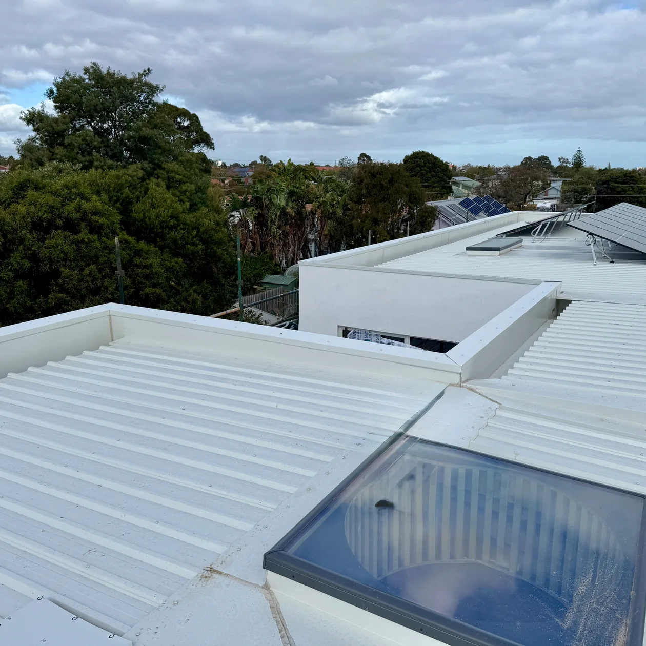 Pale metal roof with parapet walls and a roof window on a modern home