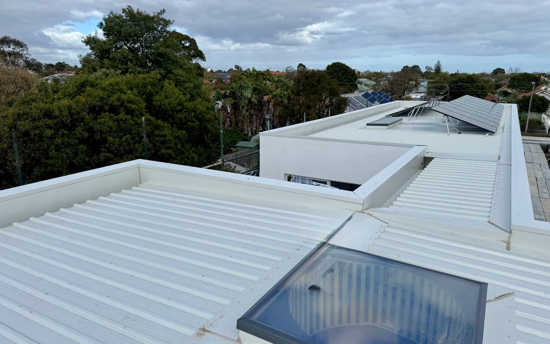 Pale metal roof with parapet walls and a roof window on a modern home
