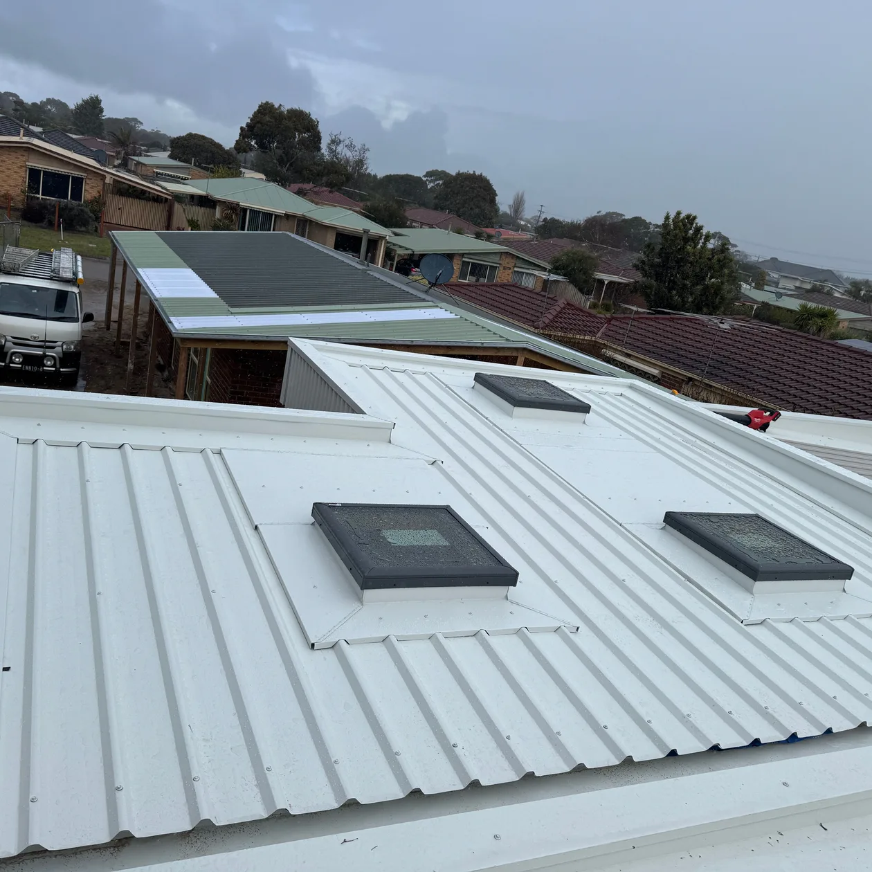 Pale corrugated metal roof running up to a scaffold rail beside neighbouring homes