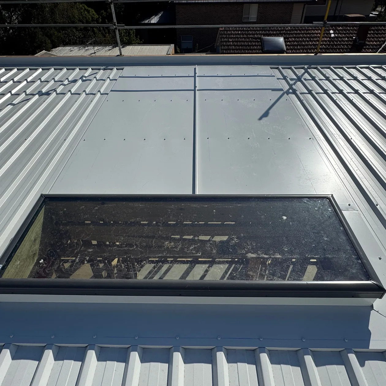 Pale metal roof with a large roof window set into long flat metal sheets