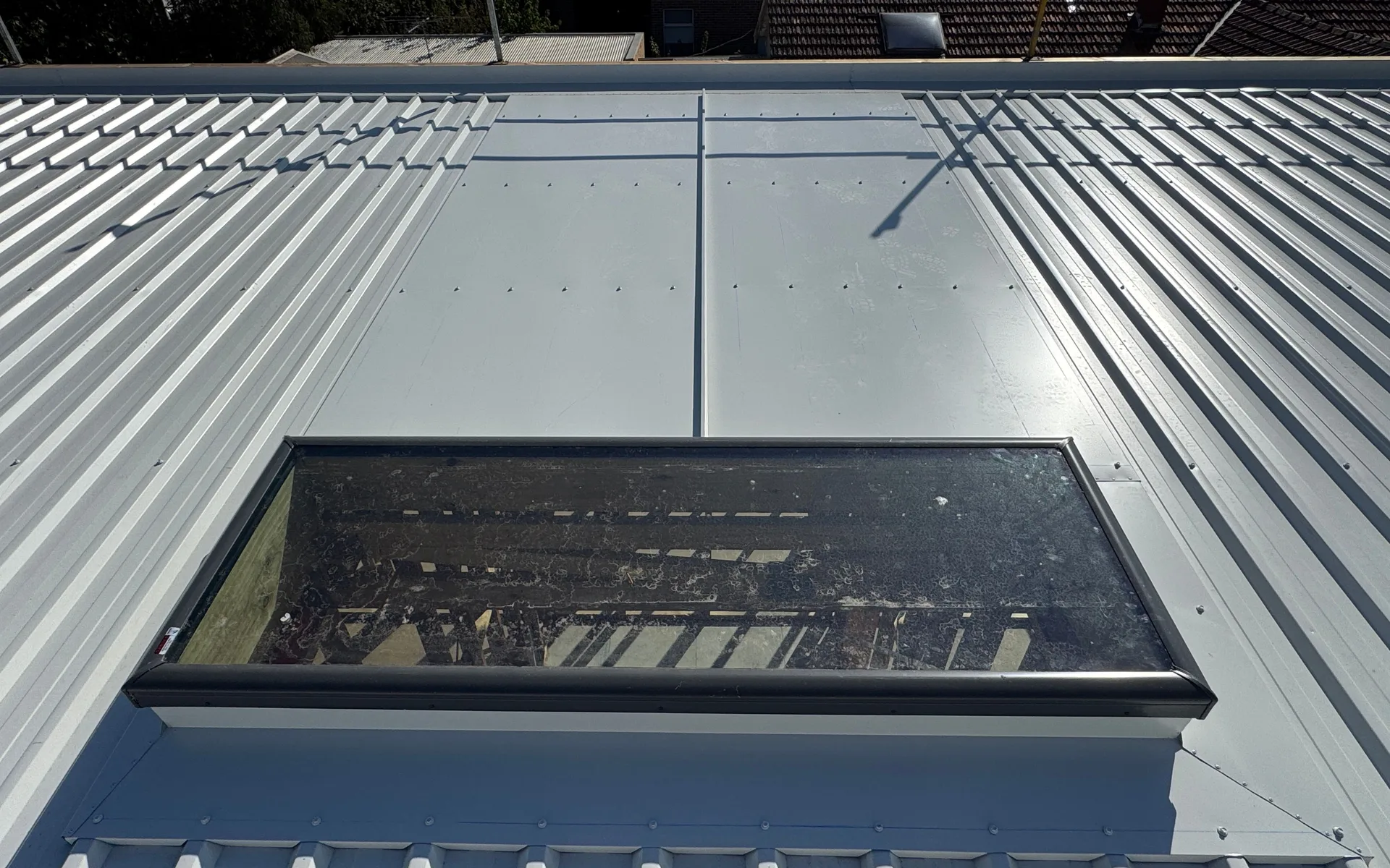 Pale metal roof with a large roof window and long metal sheets